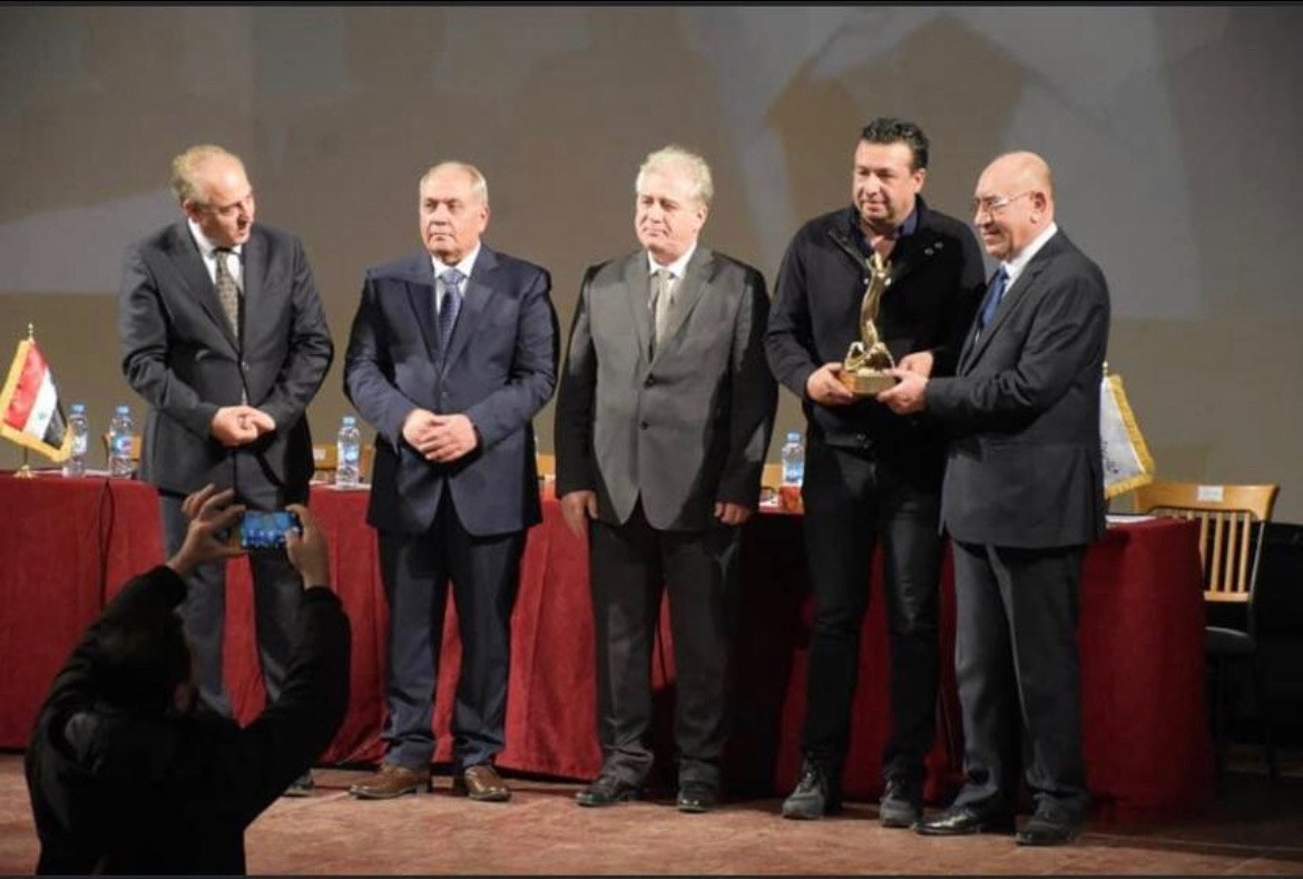 Alaa Hajjo receives an award from the Syrian Chamber of Industry on stage.